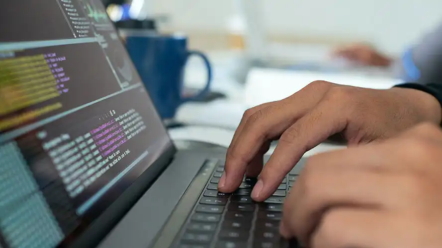 Typing on a laptop, programming code is displayed on screen.